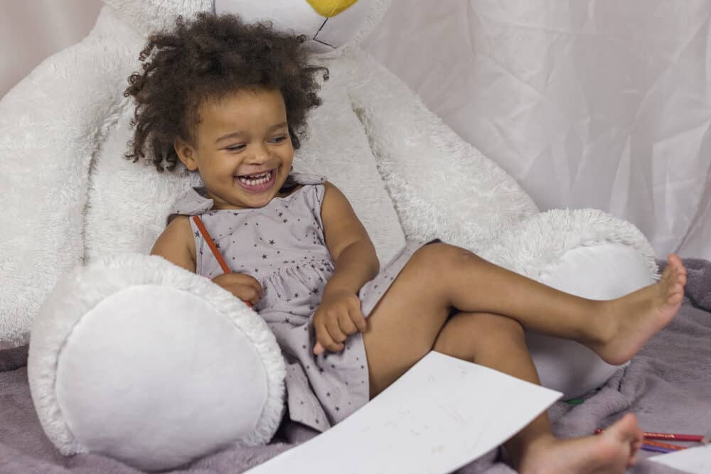 Cute little toddler laying stuffed bear drawing a picture with a colored pencil