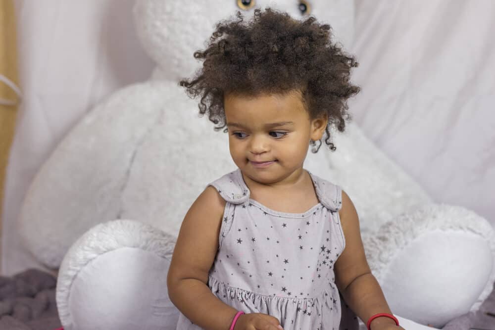 Cute toddler girl with huge, brown eyes looking down playing with silly putty