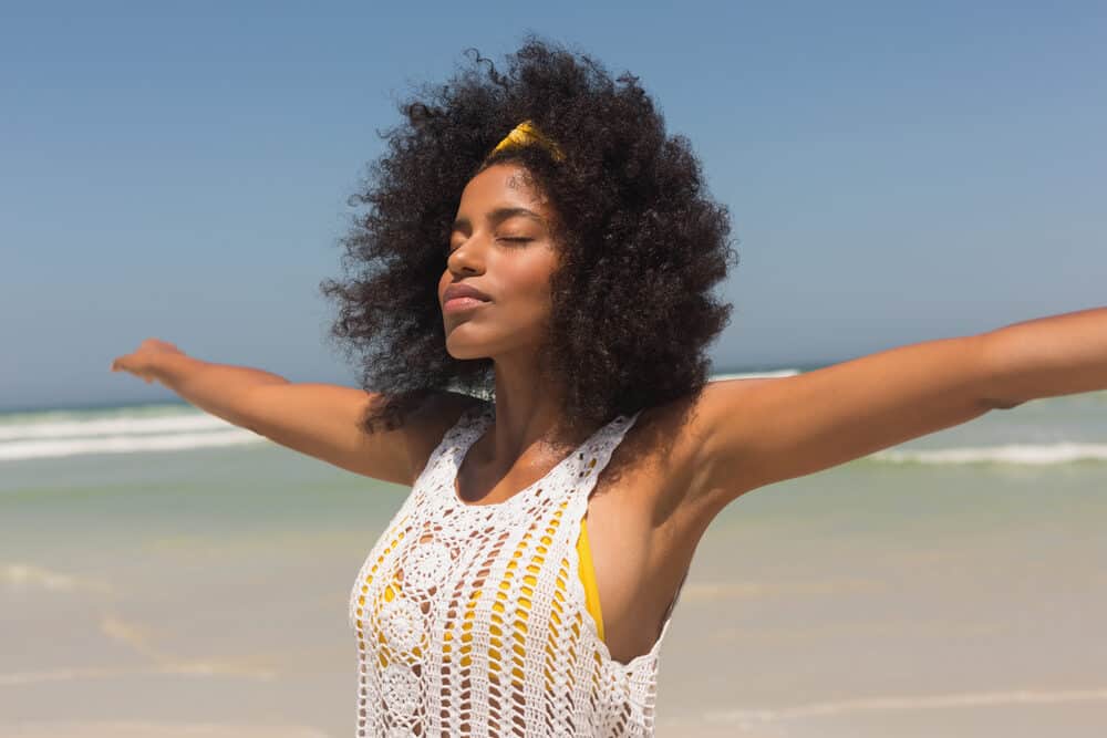 A woman at the beach twirling to remove the remaining sand from her hair