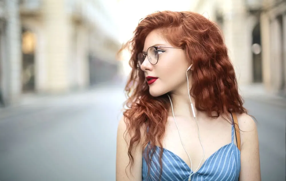 Female with very long hair wearing a blue dress while listening to music with white earphones.