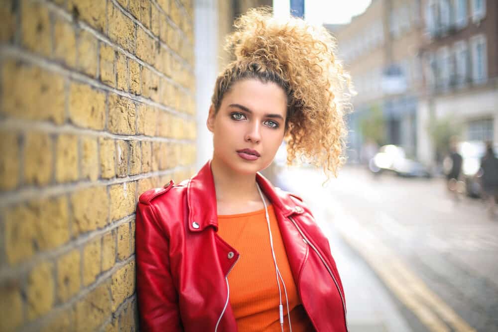 Cute white girl with golden highlights on color-treated hair wearing a red leather jacket and orange shirt