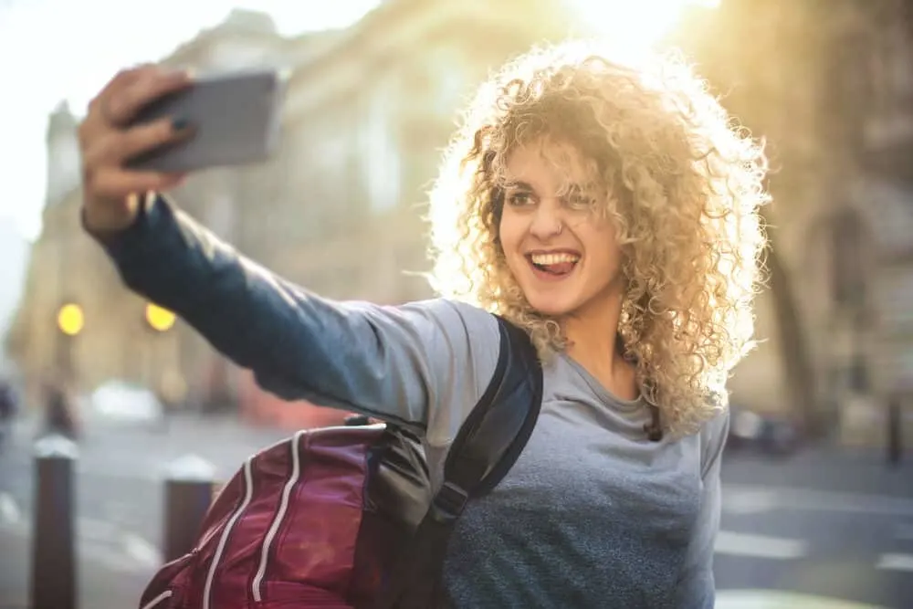 Wella T14 vs T18: What’s the Difference? Can You Use Both? Results and More. 10 A beautiful girl is taking an awesome selfie of herself with darker roots and blonde waves.