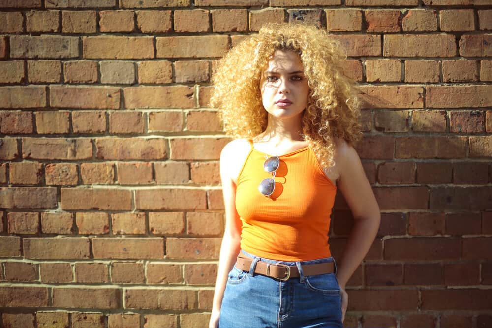 An attractive woman standing outside near a brick wall while soaking up the UV rays with a brassy color hair dye