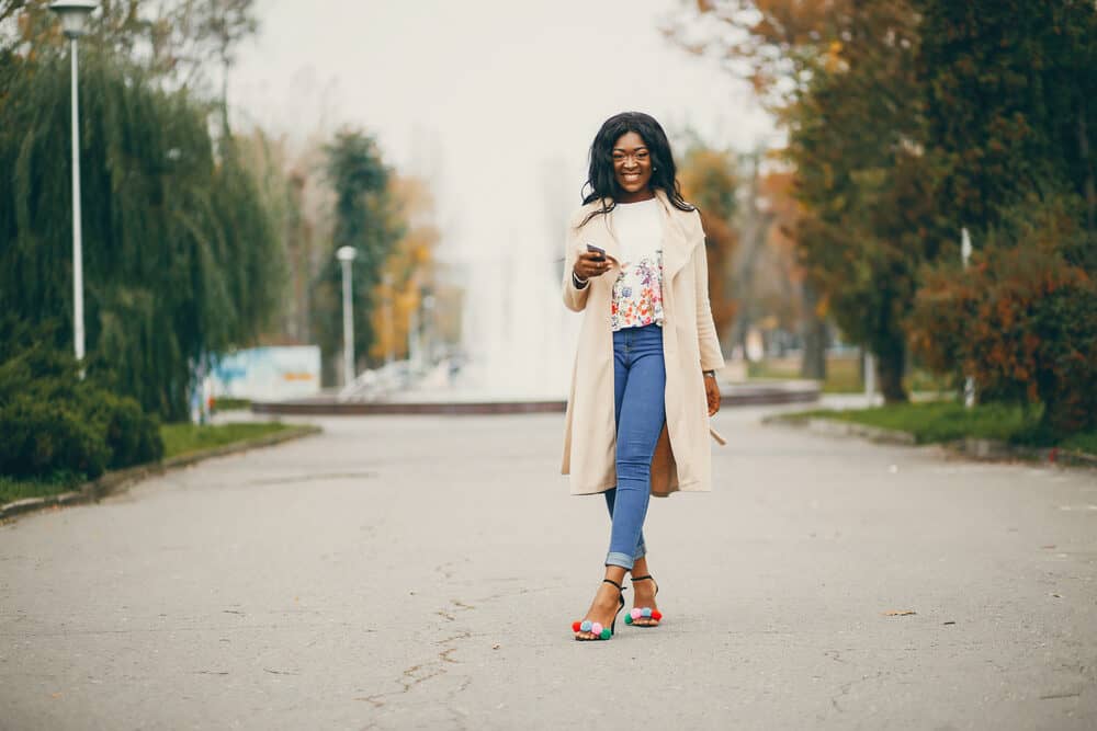 Black woman wearing a shirt with flowers, blue jeans, and a beige coat