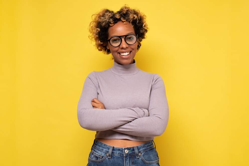 Cute black girl wearing a gray shirt, blue jeans, and black glasses.