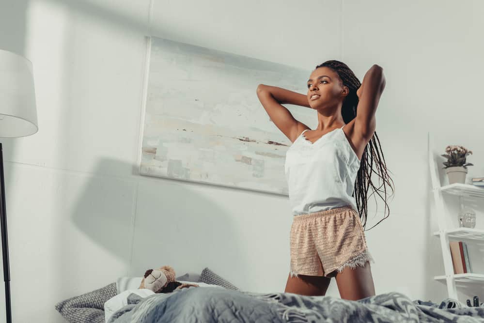 African American lady putting hair oil on her braids as she prepares for bed.