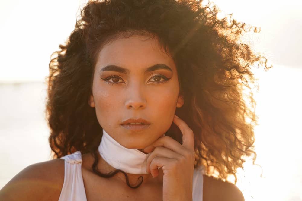  Jolie fille colombienne aux cheveux ondulés fraîchement lavés portant un débardeur blanc.