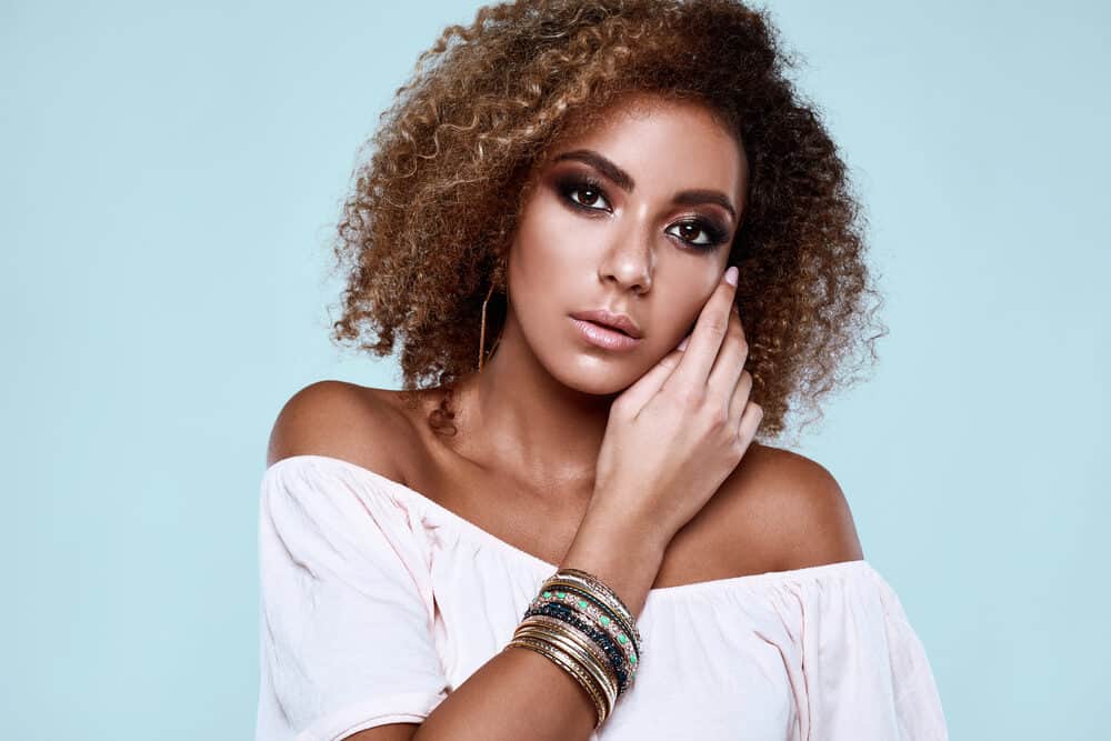 Elegant black woman with wavy curl type and medium hair thickness wearing a pink shirt and multiple bracelets