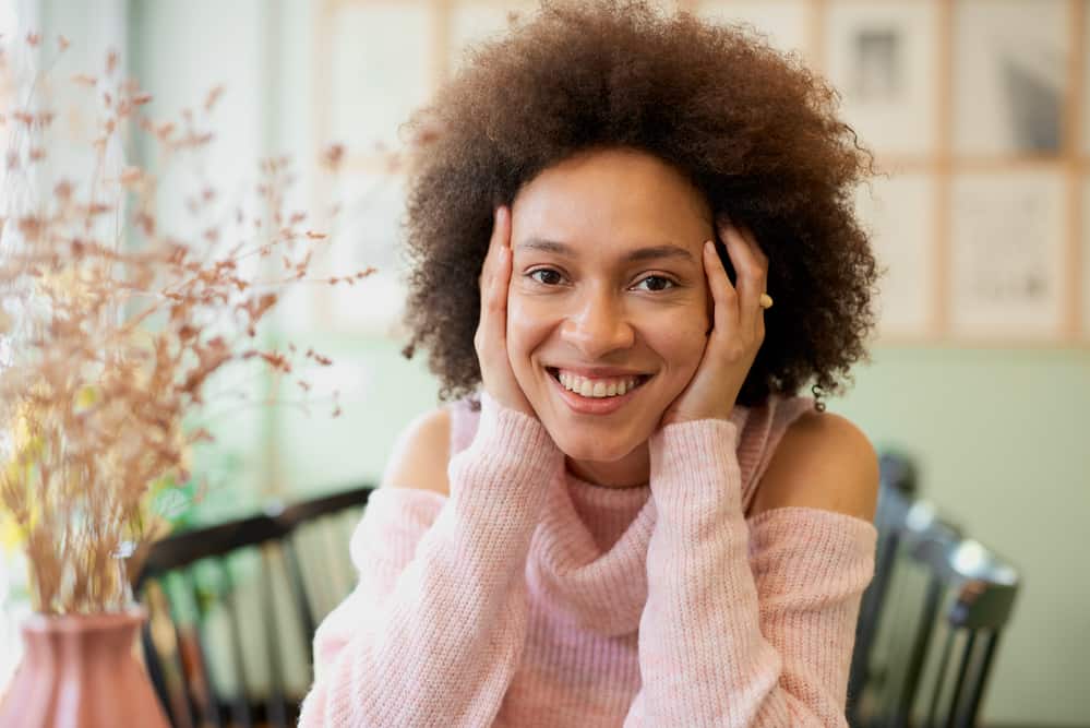 Mixed race woman with oily hair wearing a pink and white sweater