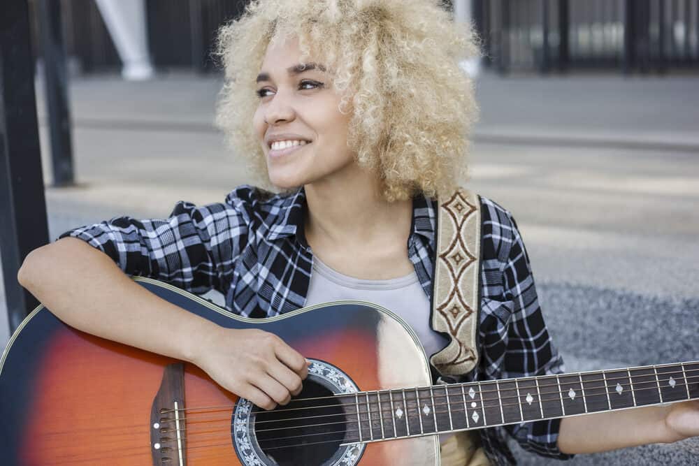 Cheerful woman with dark bleached hair smiling at the crowd while playing the guitar