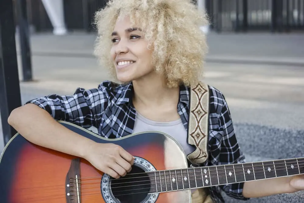 Putting Ash Blonde Over Bleached Hair: Can You Do It? What Happens? 3 Cheerful woman with dark bleached hair smiling at the crowd while playing the guitar