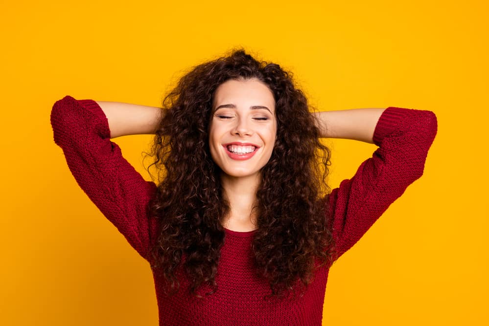 Lady with a huge smile wearing a spiral perm on virgin hair with her arms behind her head