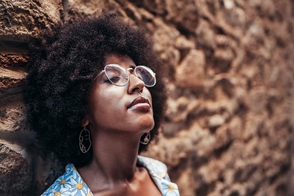Lady relaxing against a stone wall wearing her hair in afro style after using hair strengthening oil