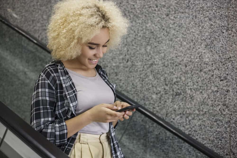 Beautiful African American woman at the mall with yellow hair toned with purple shampoo riding an escalator 