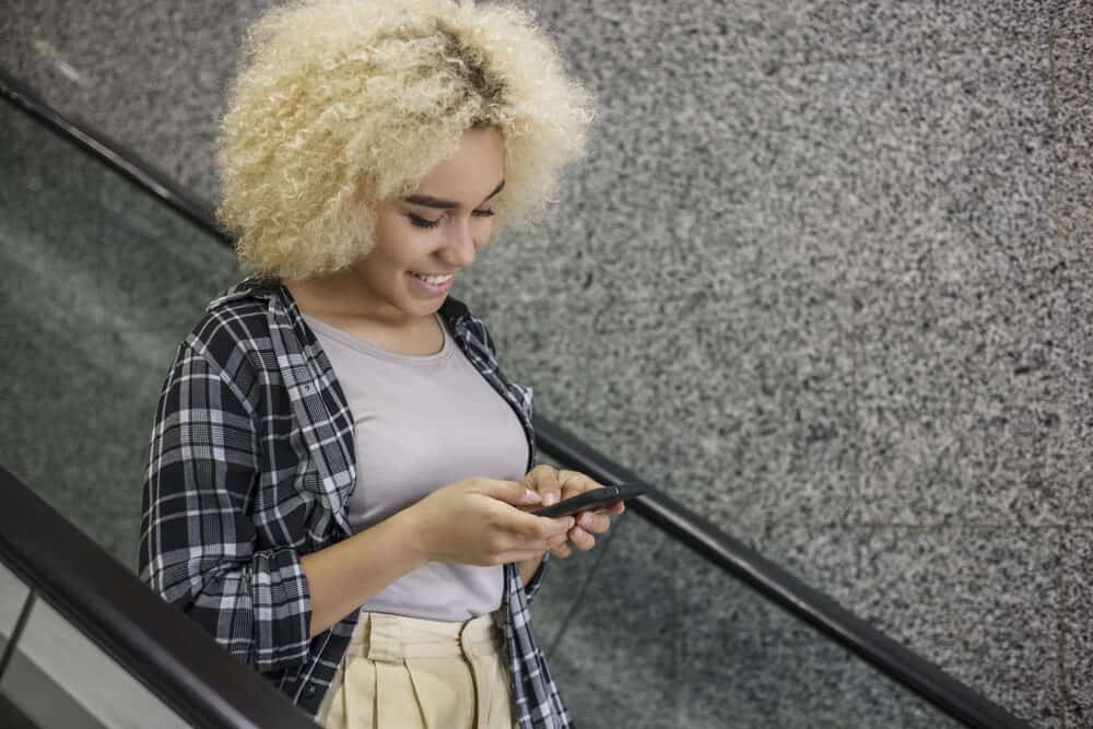 Beautiful African American woman at the mall with yellow hair toned with purple shampoo riding an escalator