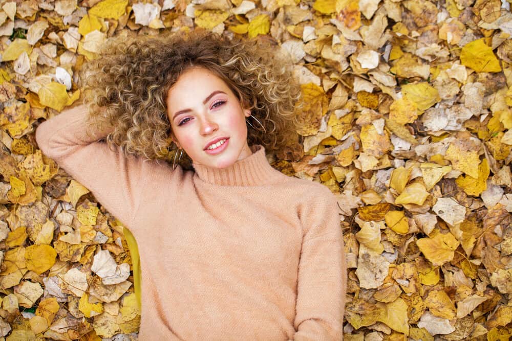 Young lady laying in brown and yellow leaves with wavy short hair