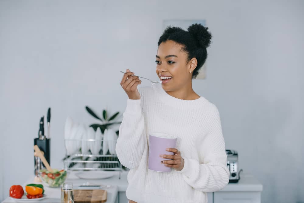 Lady wearing a white sweater while eating ice cream from a bowl