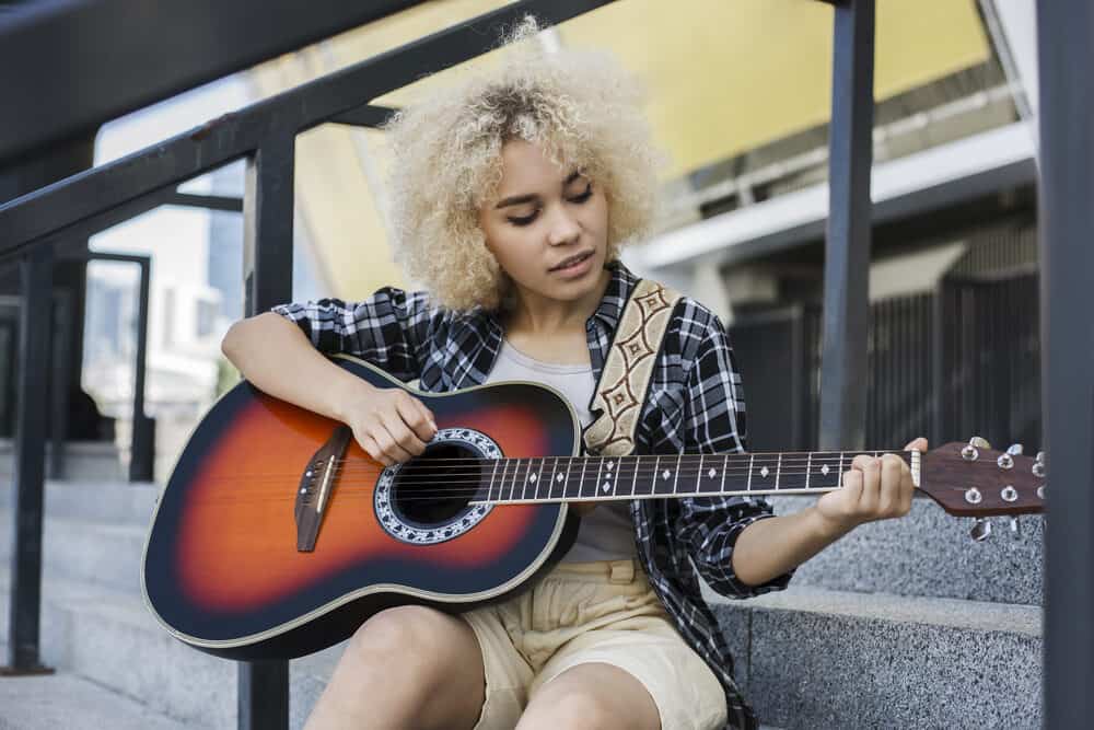 A cute black lady wearing a plaid shirt and khaki shorts with curly hair that's an ash blonde color