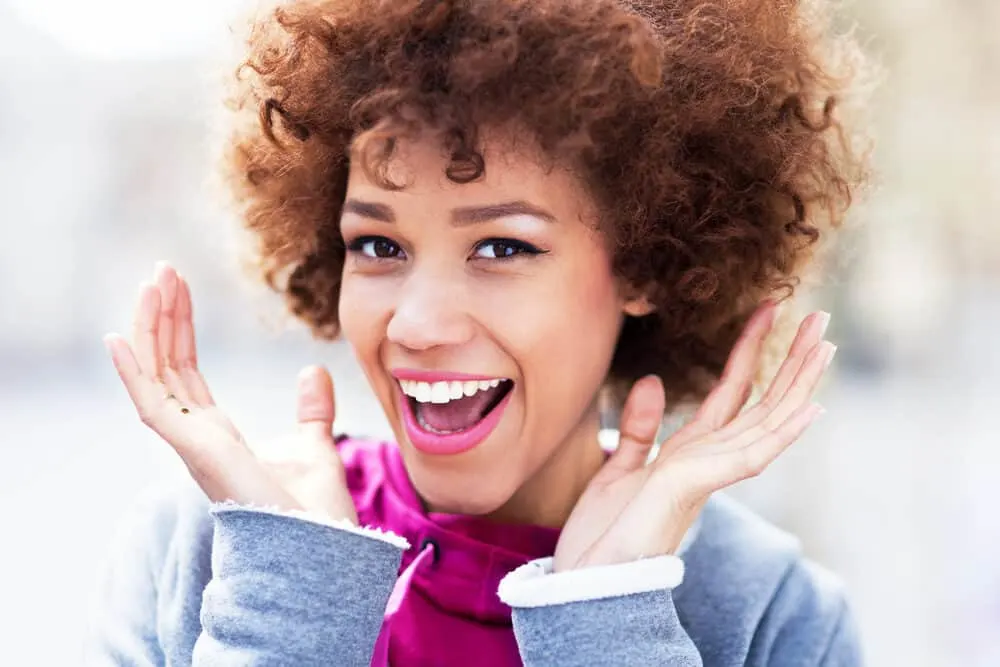 The Best Purple Hair Dye for Dark Hair Plus Alternatives 10 Black woman wearing a dark purple shirt, brunette hair, and dark violet lipstick