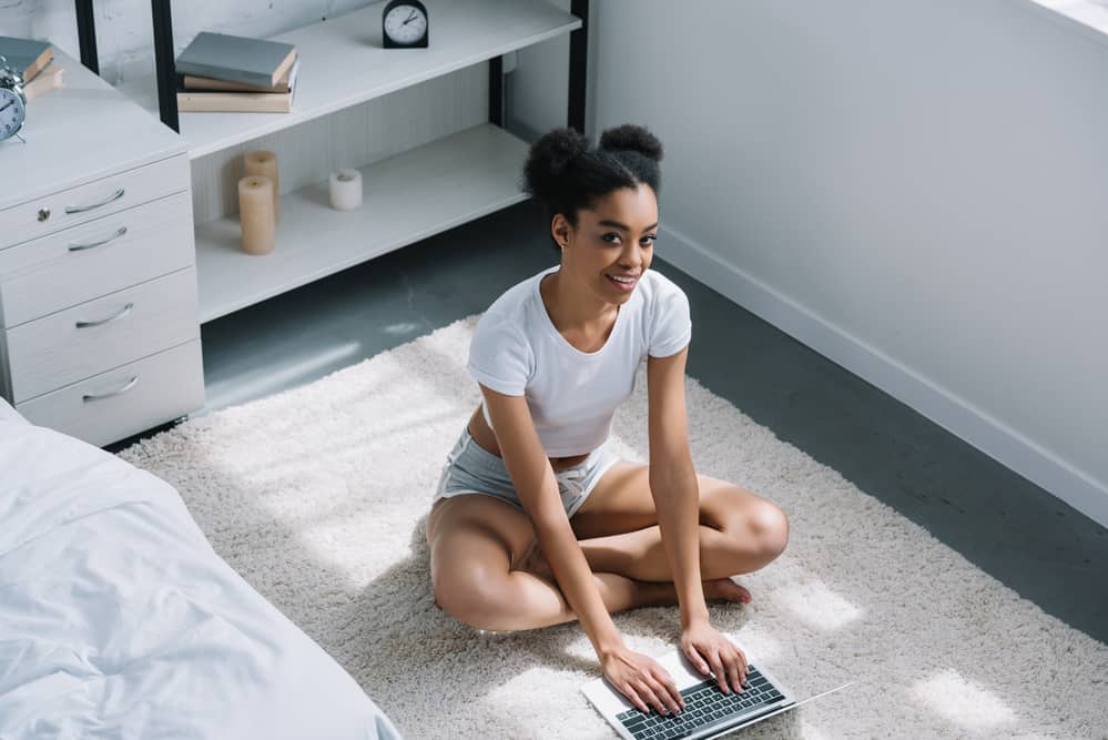 Beautiful black woman using her computer on the bedroom floor