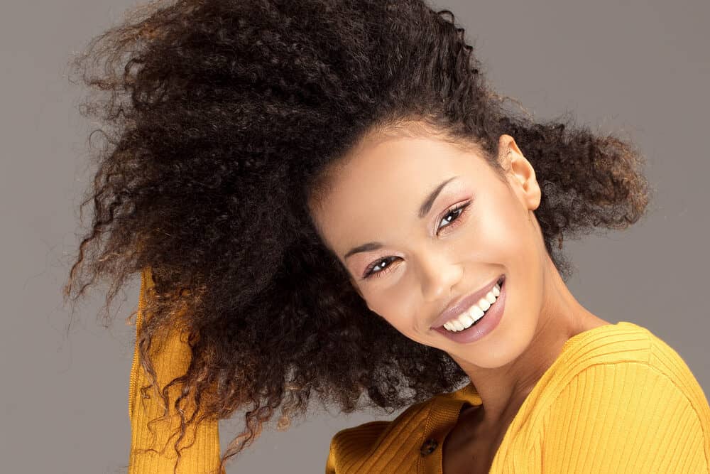 African American female wearing a yellow shirt and burgundy lipstick with curly weave hair