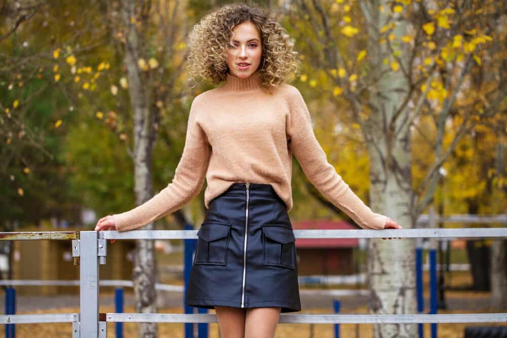 Young girl with a wavy texture hair type standing outside wearing a brown sweater and leather skirt 