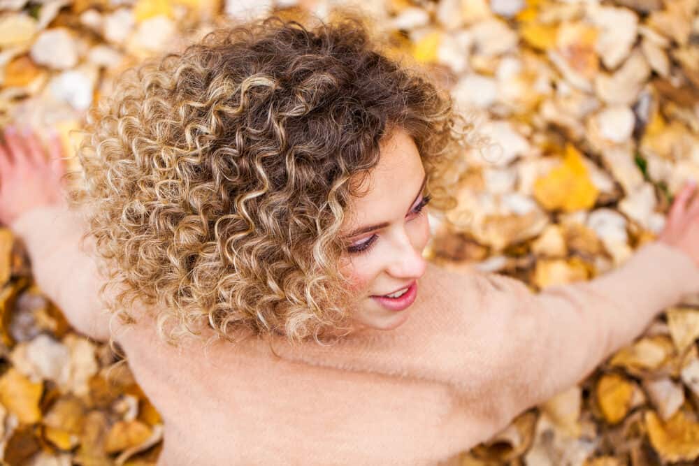 Young adult sitting in leaves on the ground while wearing a regular perm