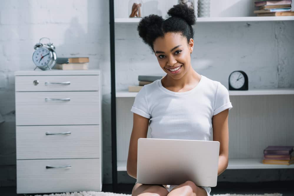 Black girl sitting on the floor using a laptop wearing the perfect afro puff hairstyle