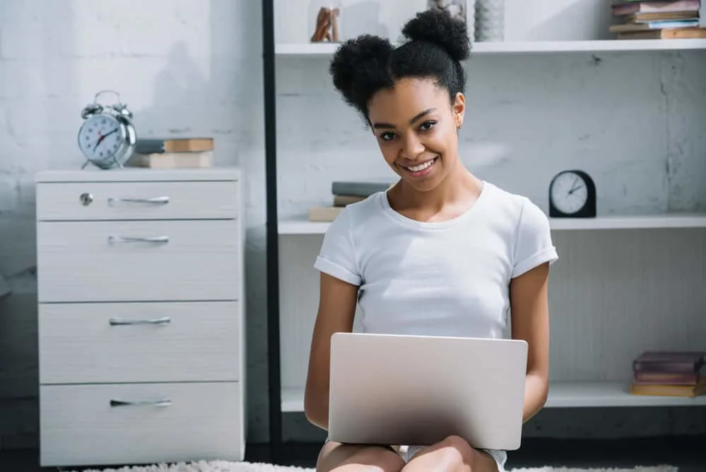 Afro Puffs Tutorial: ‘How to Do' Styling for Natural Hair: Complete Guide 3 Black girl sitting on the floor using a laptop wearing the perfect afro puff hairstyle