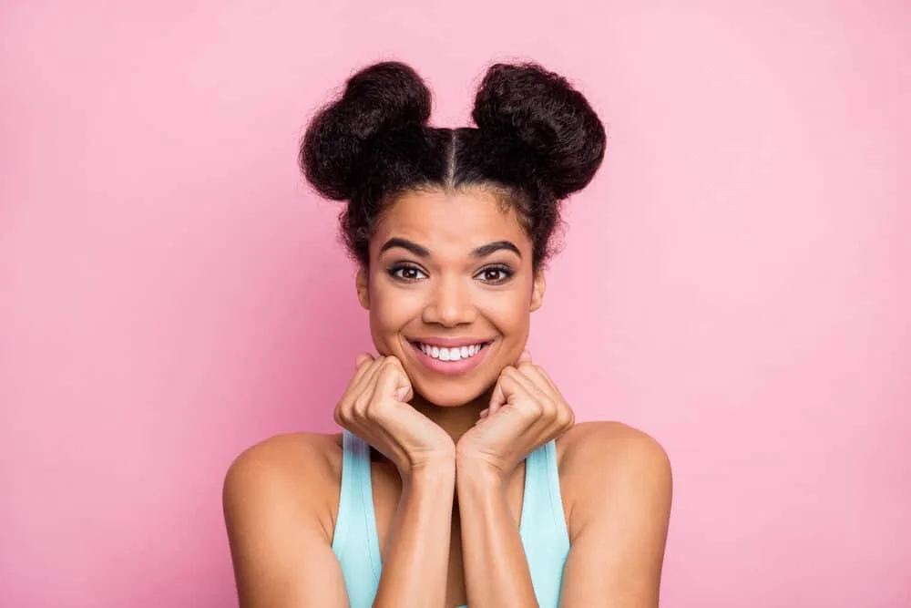 Lady wearing two small space buns with a center part secured with clear hair elastics