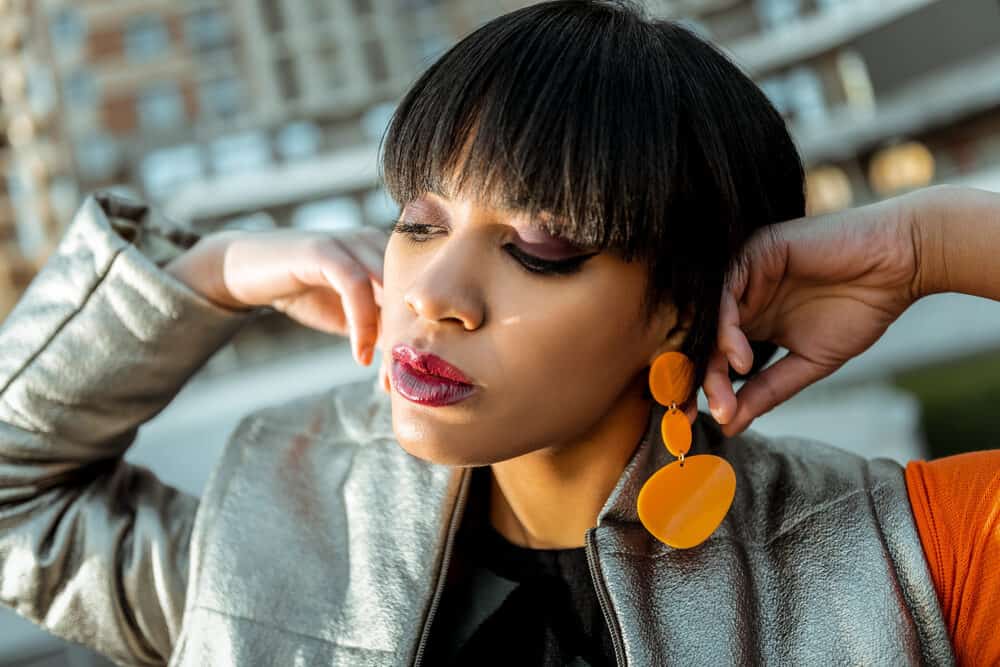 Dark-haired lady with a bad haircut with existing layers wearing orange plastic earrings