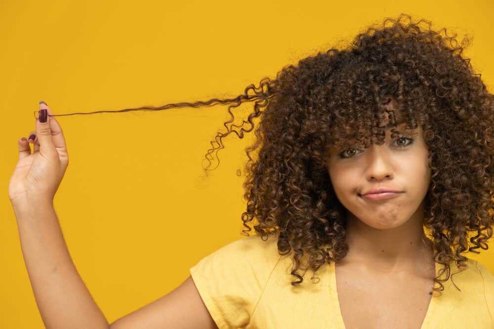 African American woman pulling her bouncy curls after using product that make her hair silky