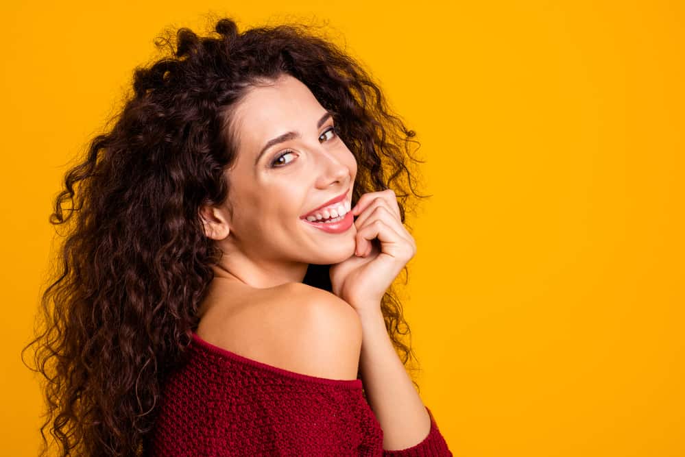 Caucasian woman with a medium hair length wearing spiral curls, pink lipstick, and a big smile