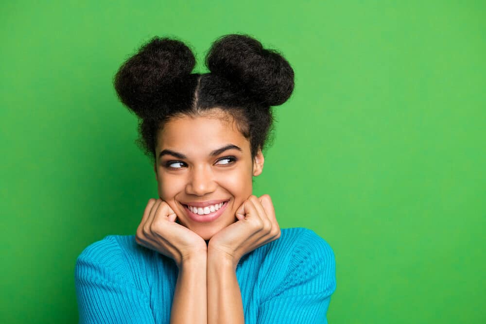 Black girl with a sneaky smile wearing half-space buns on long hair secured by a bobby pin