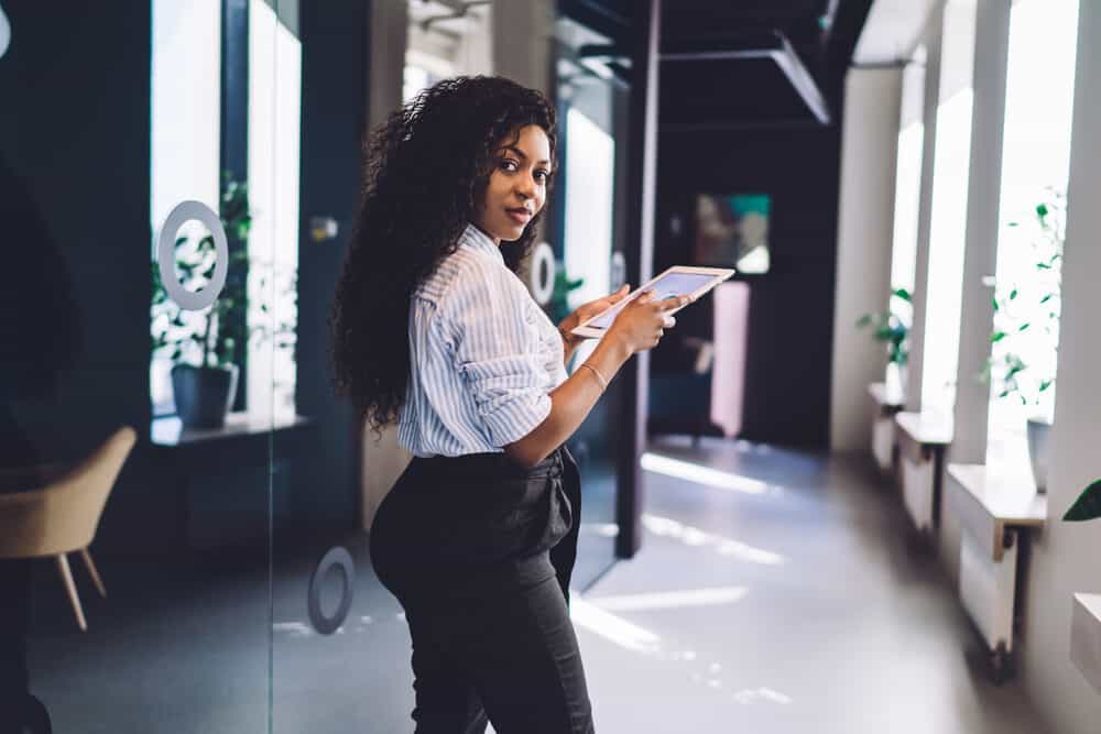 An attractive black employee with a mid-back hair length using an iPad at work