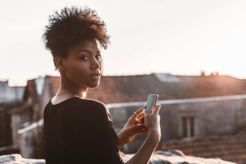 Brazilian female with oily hair standing outside using an iPhone