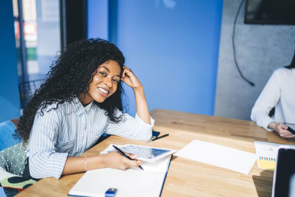 Confident female smiling while sitting at a table wearing a curly hair cut