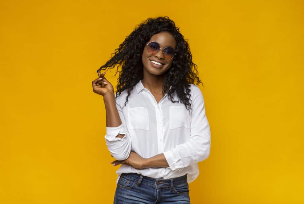 Female wearing sunglasses, a white shirt, and jeans with a wavy virgin hair bundle 