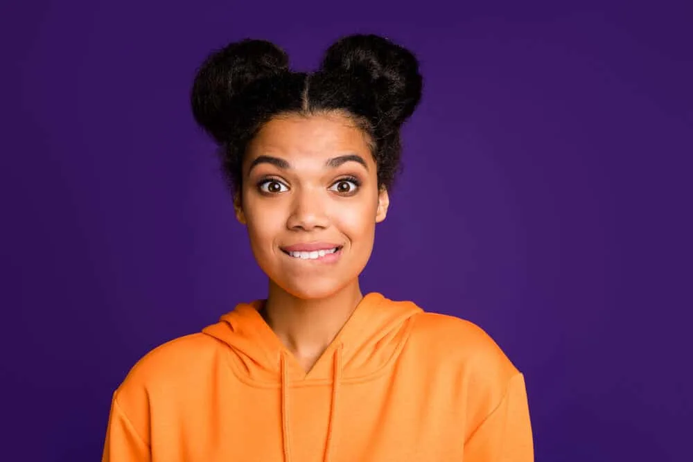 How to Do Space Buns: Easy, Step-by-Step Tutorial for Beginners 8 Black girl wearing a hoodie looking nervous while wearing a space bun style