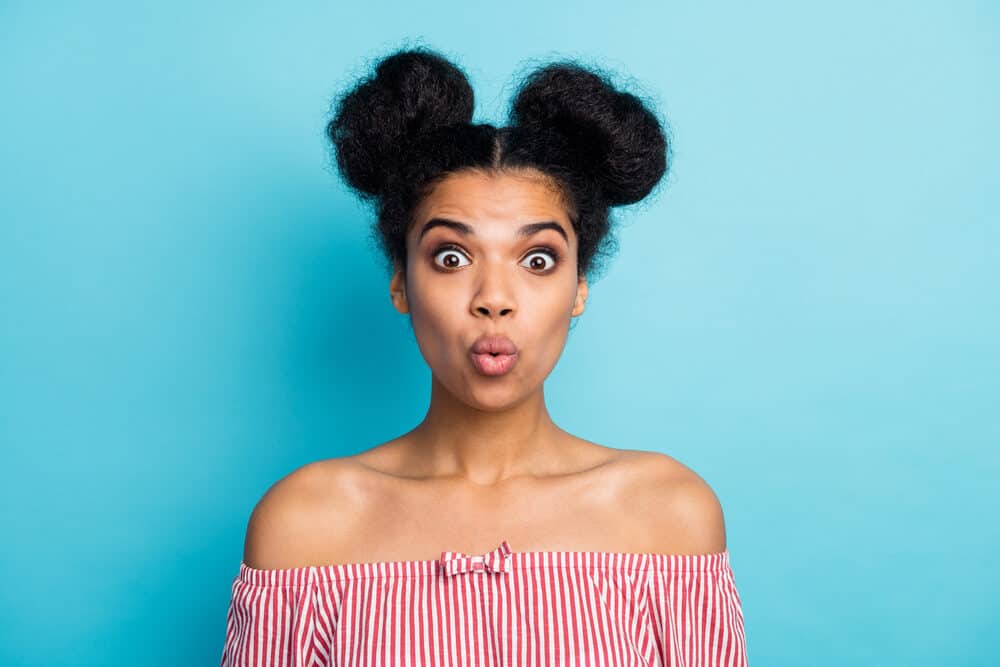 Female with a surprised look wearing a red and white shirt with double buns