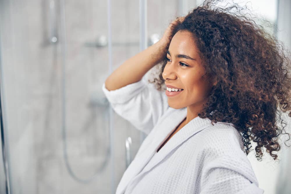 Pretty black woman with dark curly hair dried with a blow dryer adding a leave-in conditioner