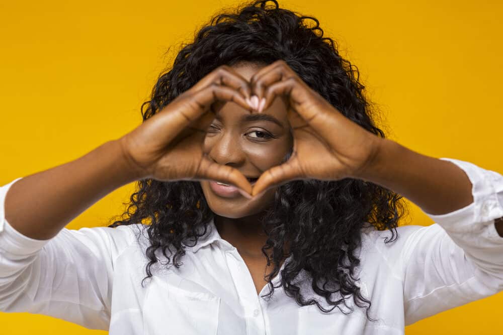 18 Cute Eye-Catching Wavy Weave Hairstyles for Black Hair 28 Black girl making a heart with her fingers while wearing deep wave braiding hair