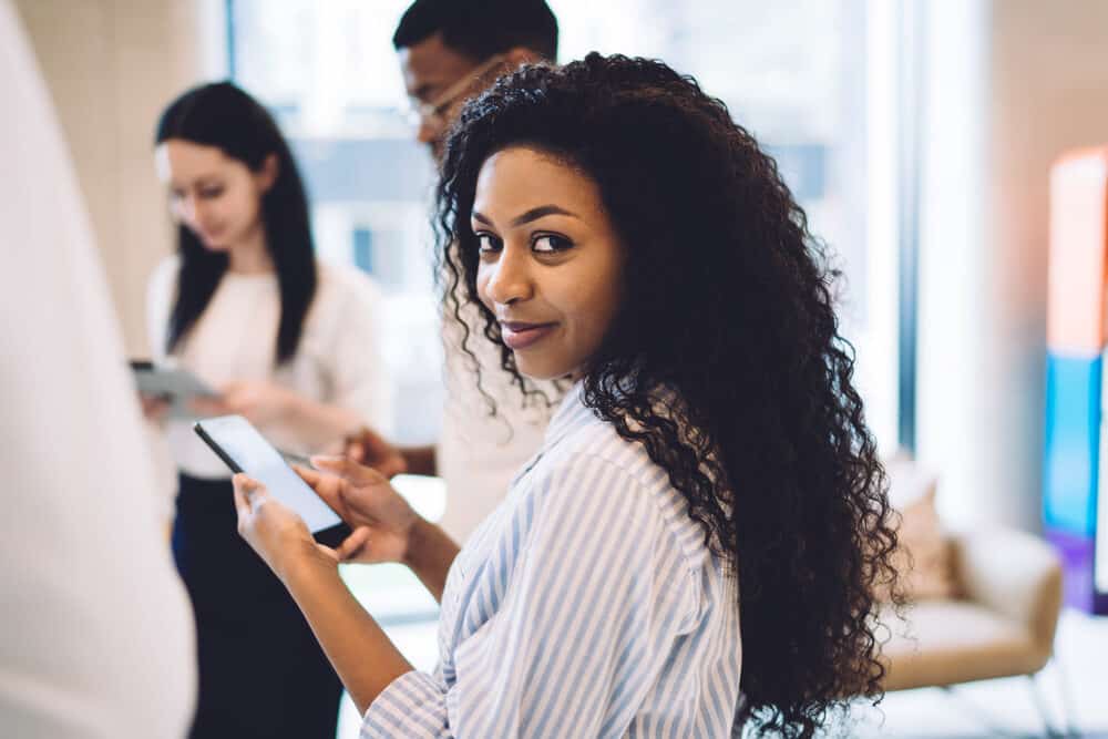 Black woman with medium length hair checking her phone at work with men and women in the background