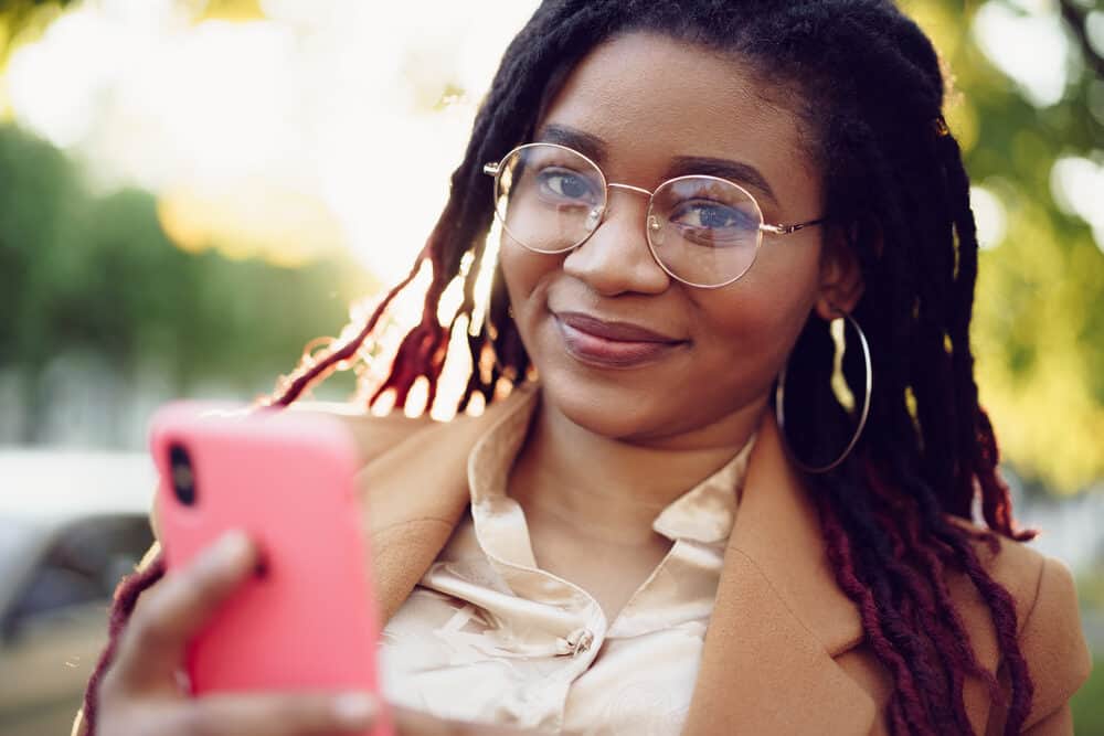 African American female wearing glasses and pink lipstick reading about interlocking maintenance on her mobile phone