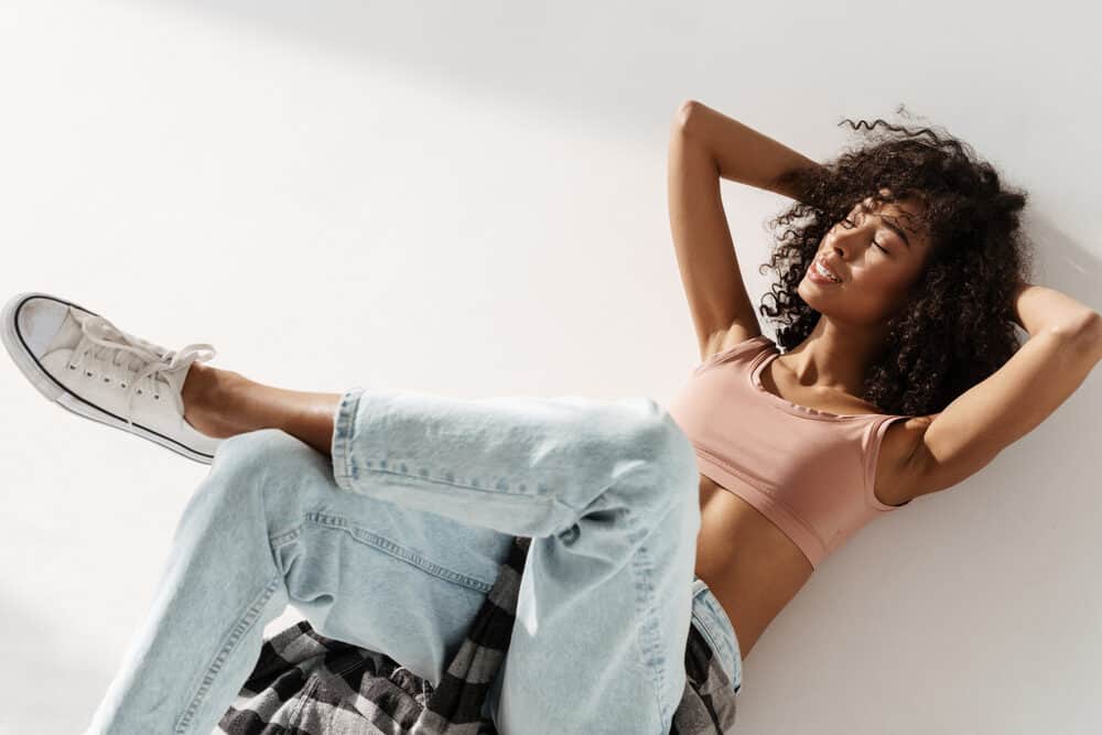 A black lady with low porosity hair leans back as a few strands of hair fly in the wind