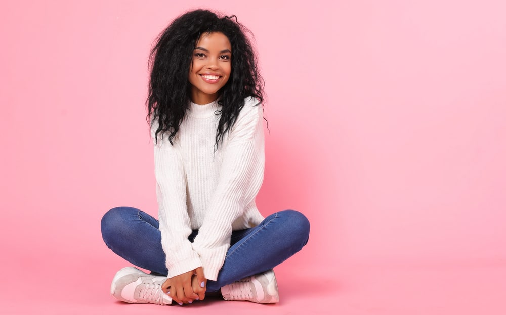 Female with a natural black hair color and medium hair length wearing a white sweater and blue jeans