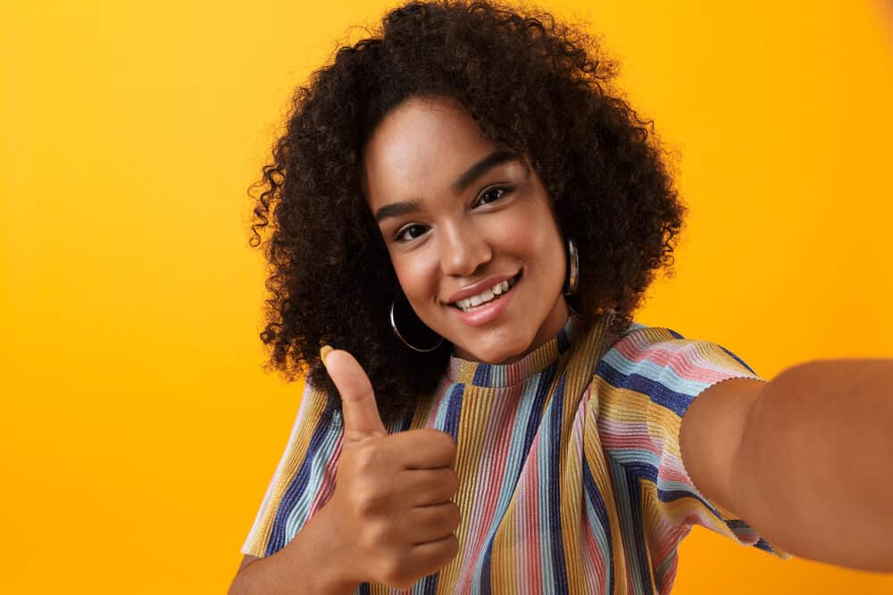 Black girl with tightly coiled knaps around her edges wearing a colorful shirt while giving a thumbs-up
