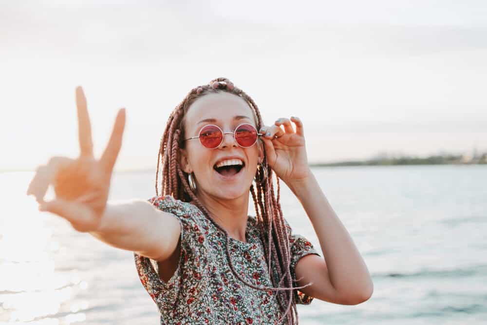 White female rocking caucasian box braids while wearing sunglasses and giving a peace sign