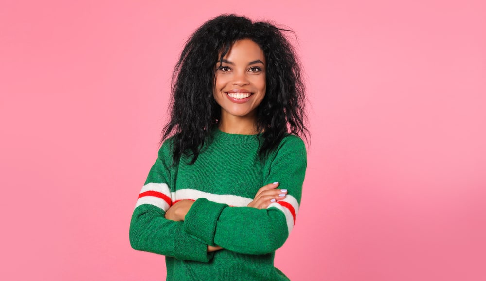 Black girl with thick and full hair wearing a green sweater with a red stripe across both arms