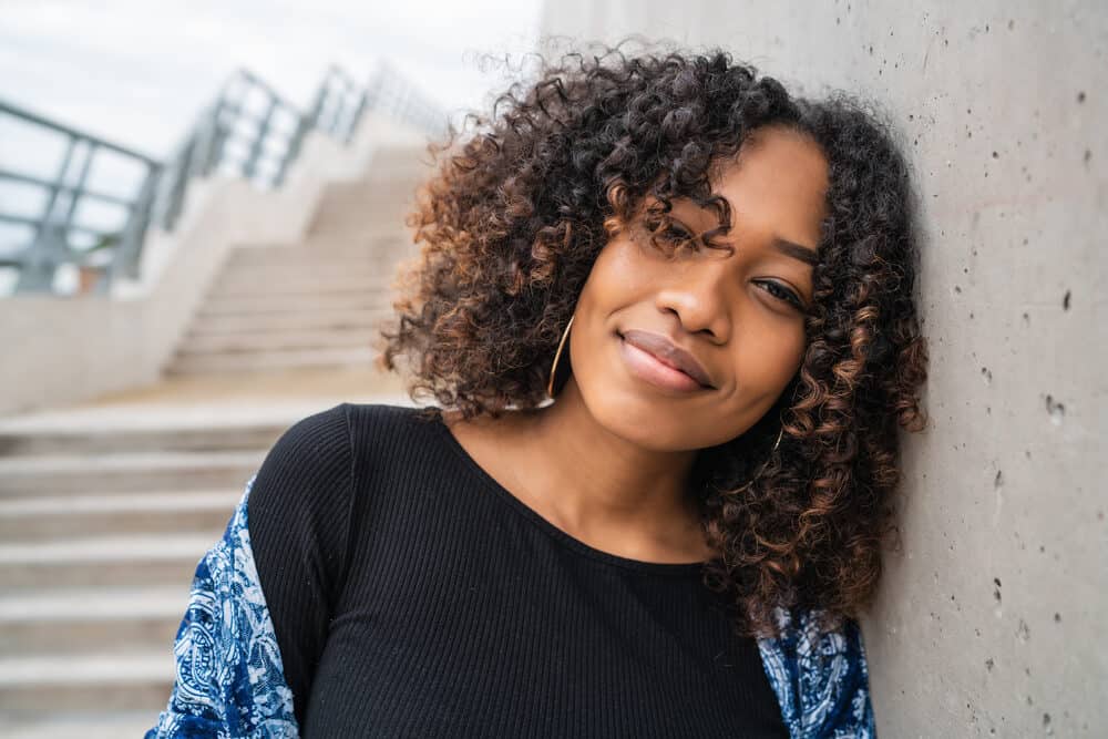 Young African American female with high porosity hair leaning against a concrete wall